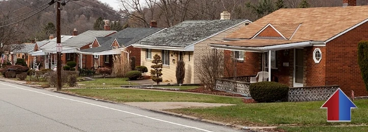 Row of single-story suburban brick homes along a quiet residential street with front lawns and leafless trees.