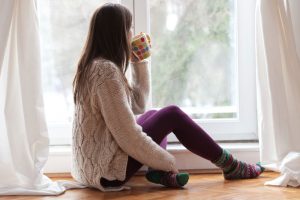 Beautiful young woman sitting by the window having hot drink