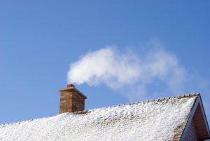 White smoke comes out of a house's chimney on a winter day.