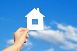 cardboard-house-cutout-being-held-against-blue-sky