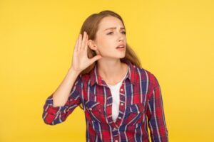 woman-standing-on-yellow-background-holding-hand-to-ear-to-listen