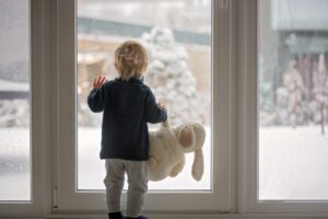 small-boy-looking-out-glass-door-at-snow-covered-backyard