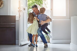 smiling-man-walking-in-house-hugging-two-kids