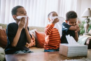 3-kids-sitting-on-couch-blowing-noses