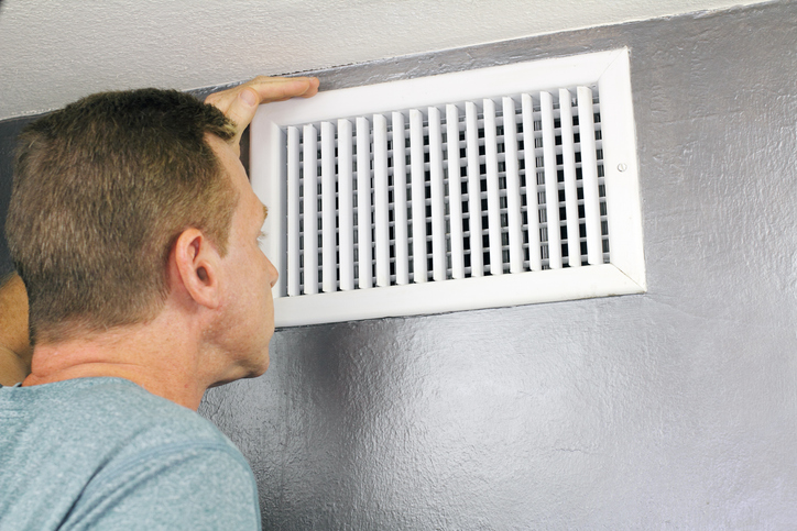 Mature man examining an outflow air vent grid and duct to see if it needs cleaning.